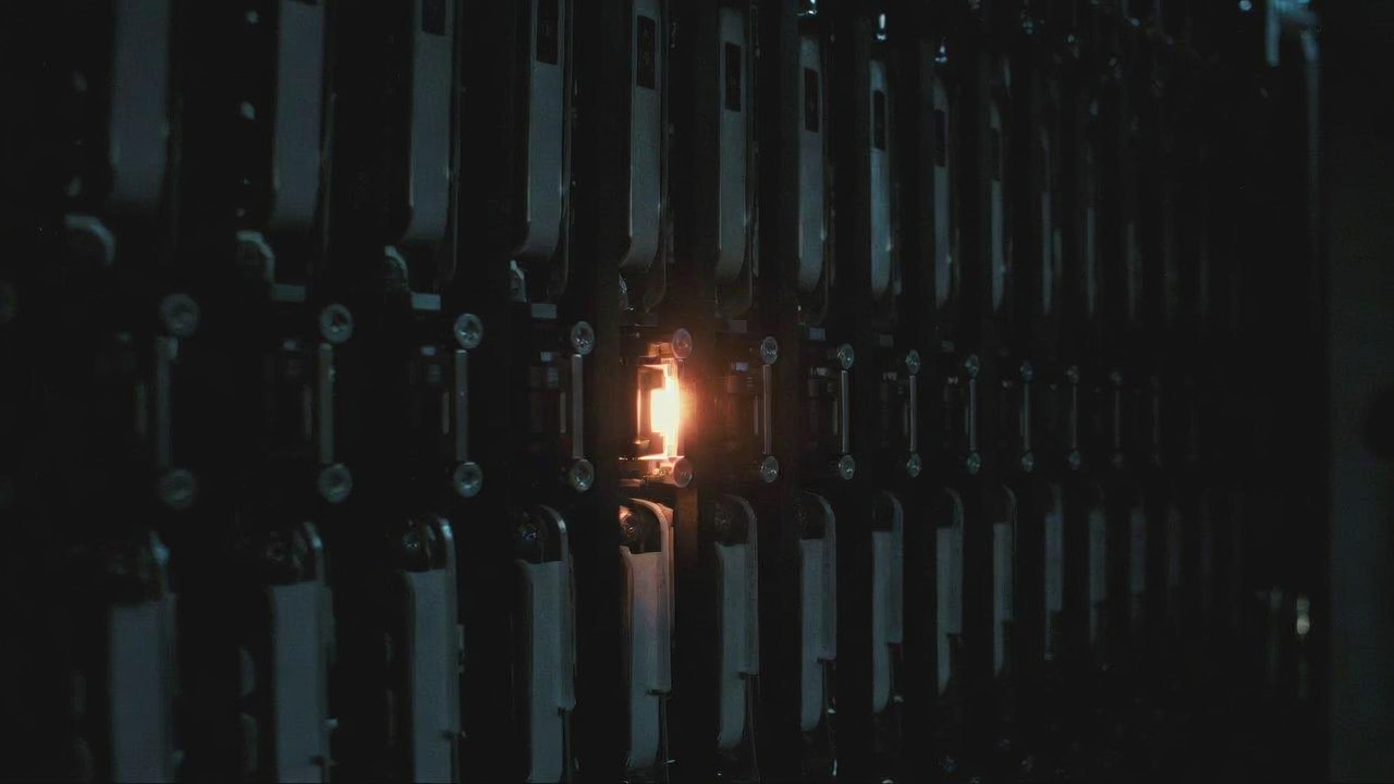Close shot of a server rack with a single blinking amber LED in an otherwise dark row.