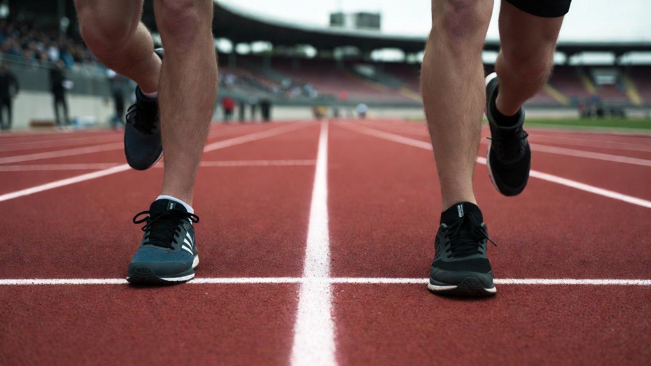 Two runners' shoes captured mid-stride at the exact same finish line, viewed straight down from above.